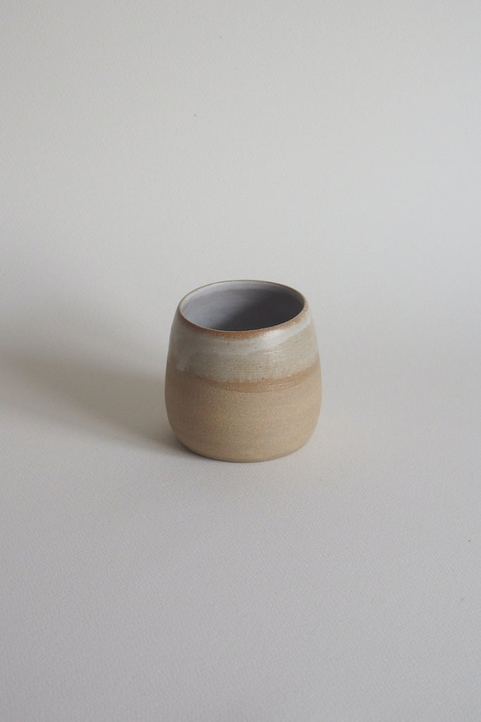 rounded tumbler, half dipped in glaze, creating different colours such as warm brown near the lip, changing slowly to a muted white
